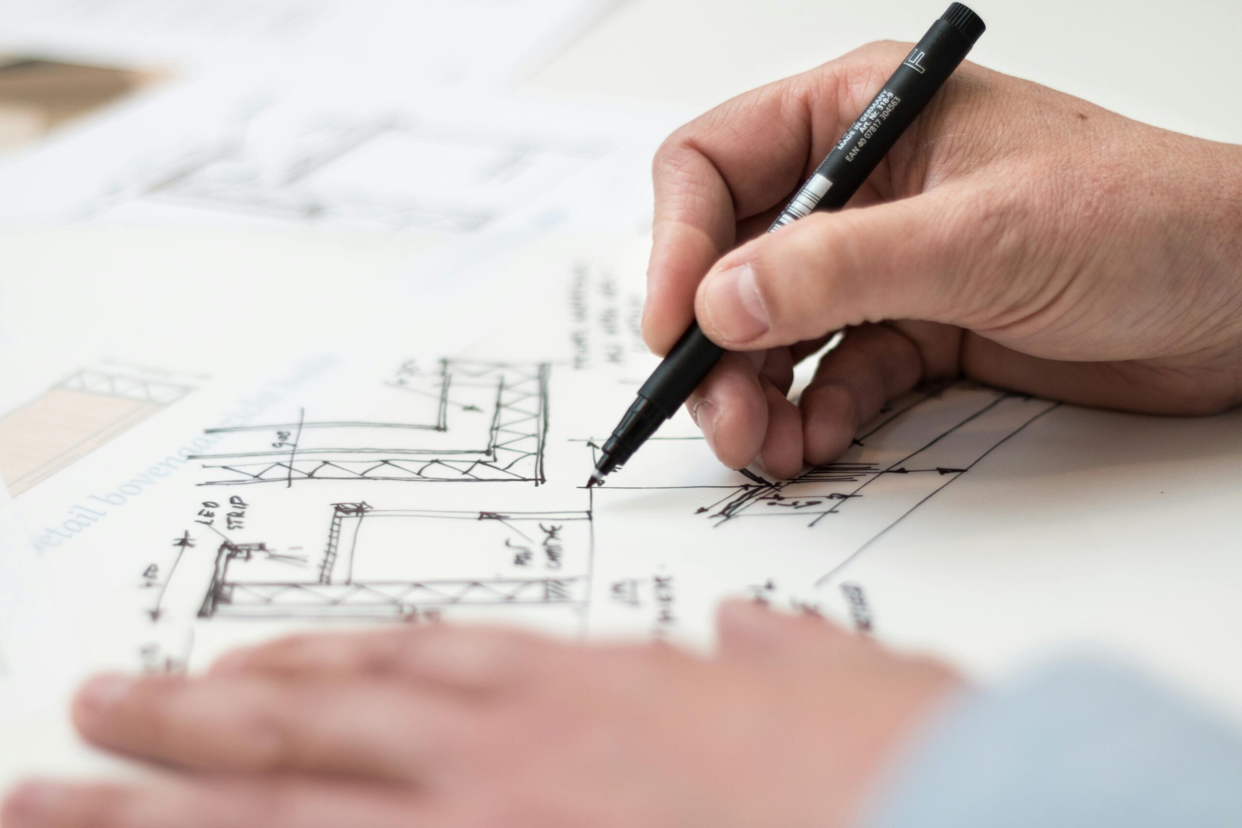 Close-up of hand drawing home plan designs on blueprint with pen, ideal for engineering or architecture themes.