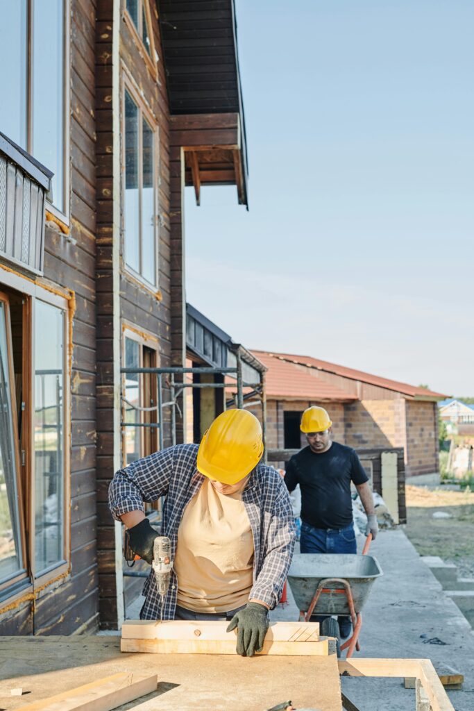 Latest Trends in Home Building and Design Two workers in hard hats engaged in carpentry at a construction site, building a wooden house.